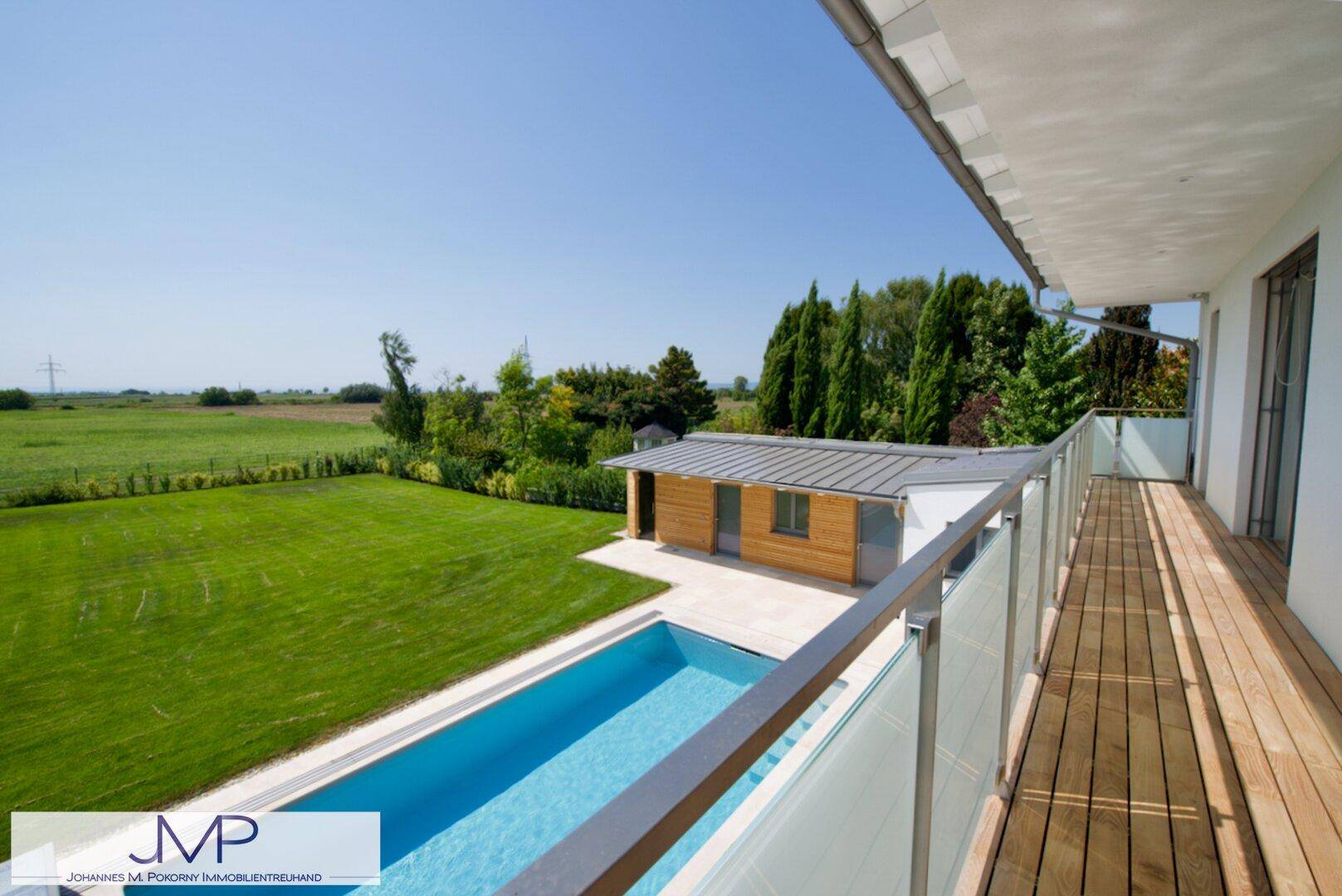 Geräumiger Balkon mit Holzbelag, Glasgeländer und weitem Blick über Garten und Landschaft.
