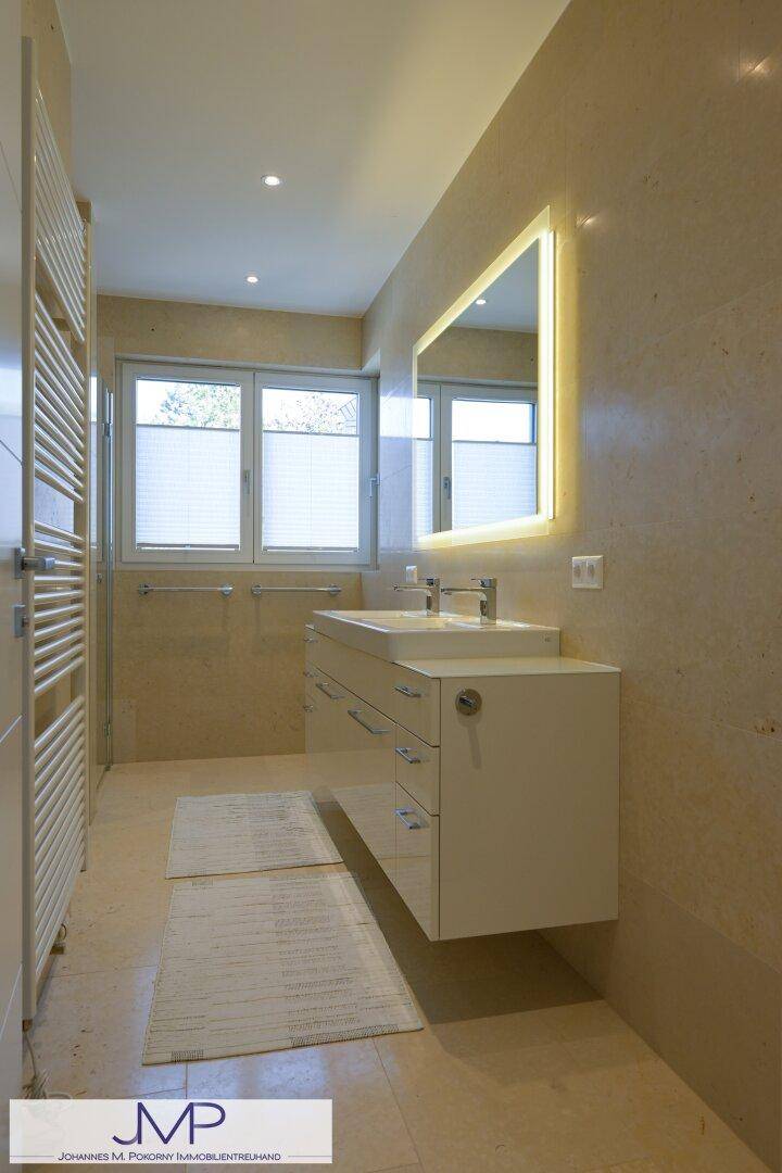 Elegantes Badezimmer mit schwebendem Waschtisch, beleuchtetem Spiegel und großen Fenstern für Helligkeit.