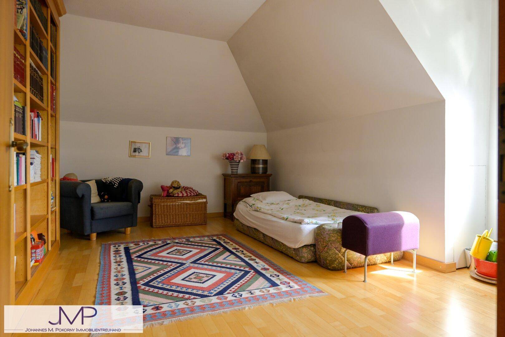 Gemütliches Schlafzimmer im Dachgeschoss mit schräger Decke, Holzboden und einem großen Bücherregal.