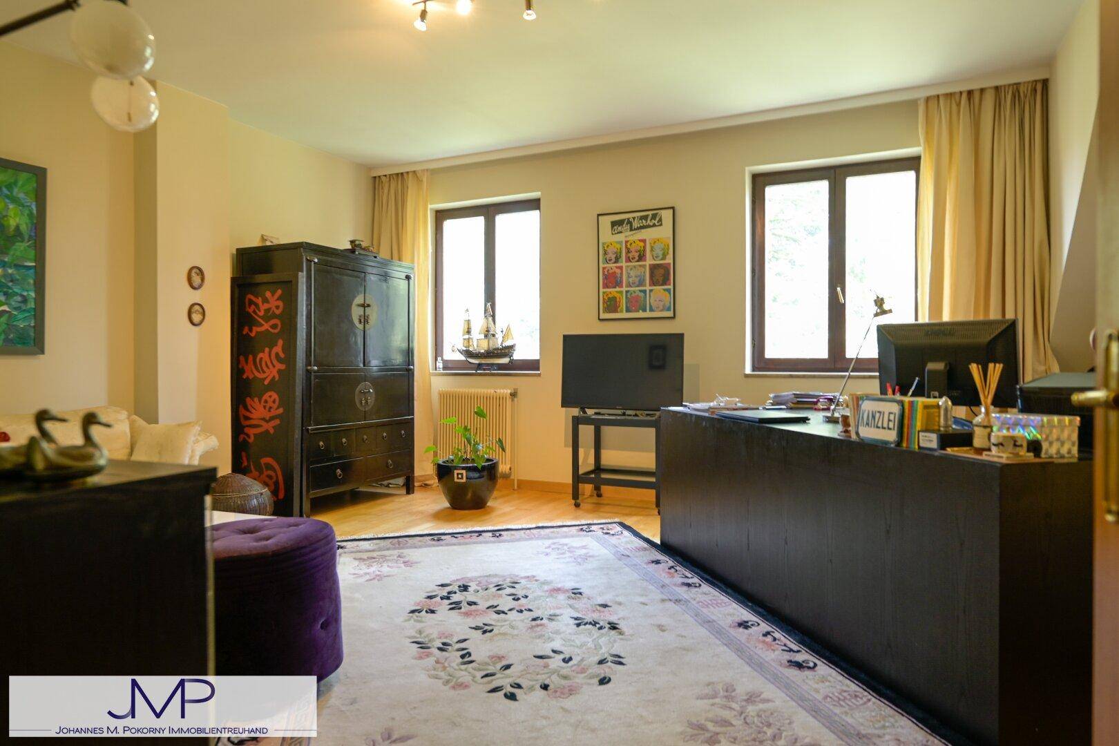 Funktionales Büro mit großem Schreibtisch, Holzboden und zwei Fenstern für ausreichend Tageslicht.