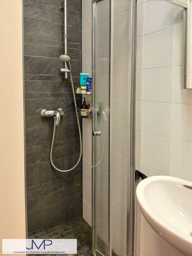 Kleines Badezimmer mit Duschkabine, weißen und dunklen Fliesen sowie einem Waschbecken.