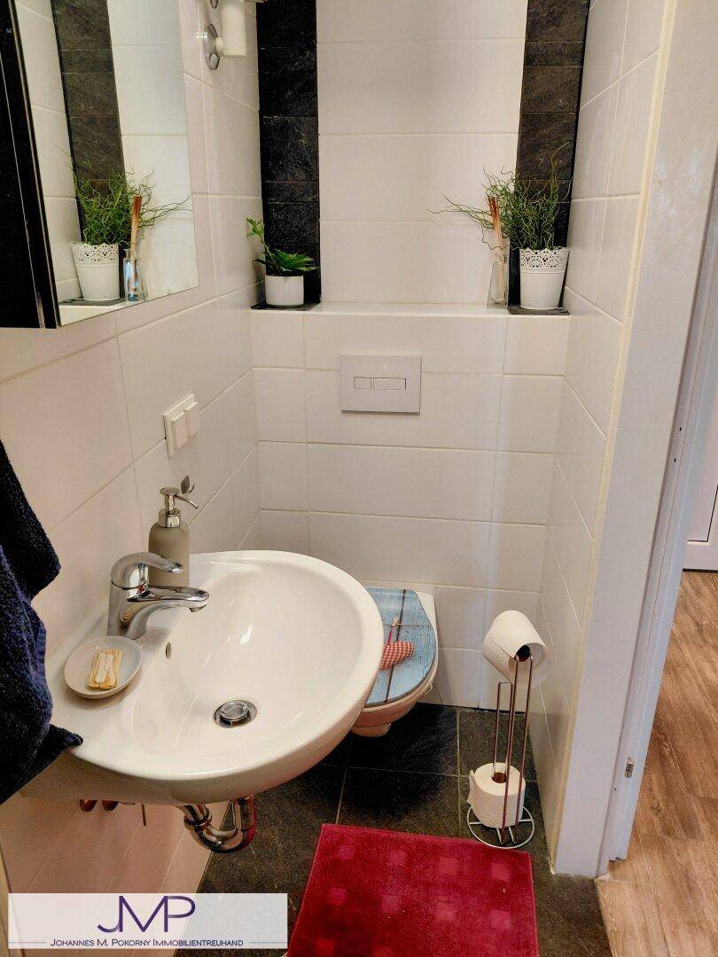 Separates WC mit kleinem Waschbecken, weißen Fliesen und Wand-WC.