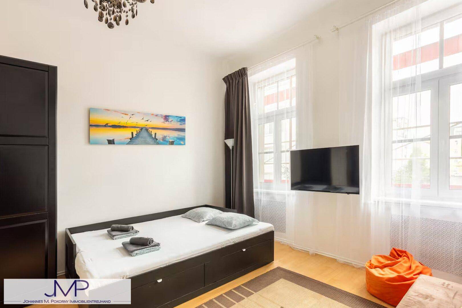 Gemütliches Schlafzimmer mit Einzelbett, Fernseher und großen Fenstern.