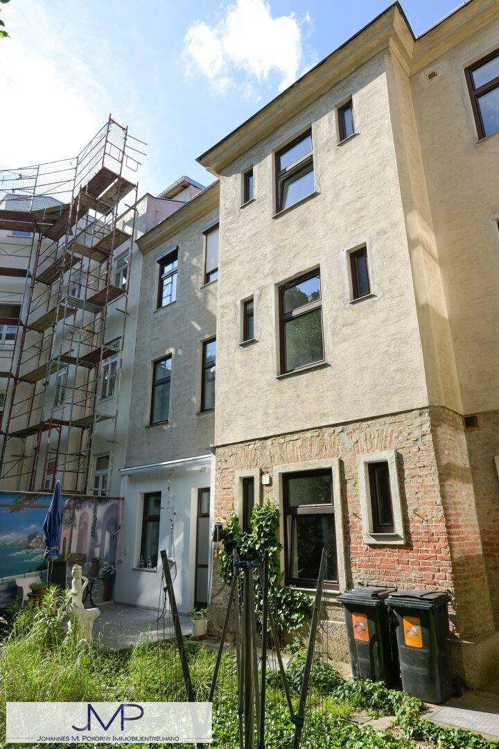 Seitenansicht des Gebäudes mit Gerüst an der Fassade und einem kleinen Gartenbereich im Vordergrund.