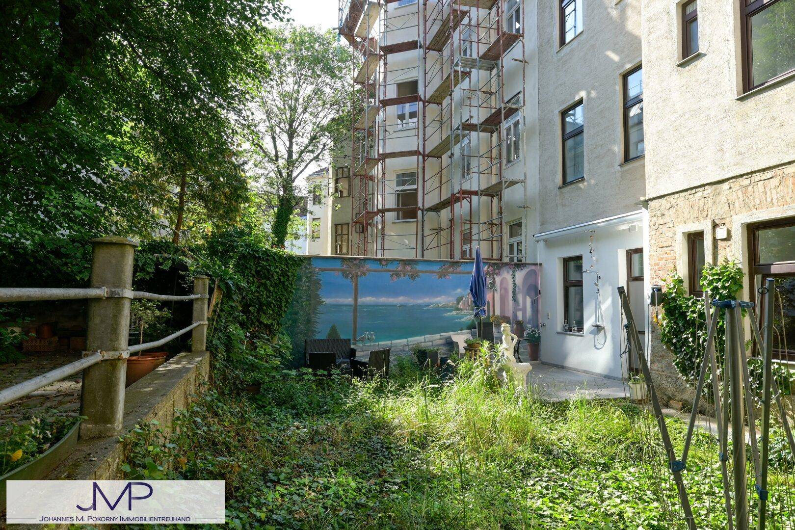 Hinterhofgarten mit Wandgemälde, Sitzbereich und üppiger Vegetation, ideal zum Entspannen.