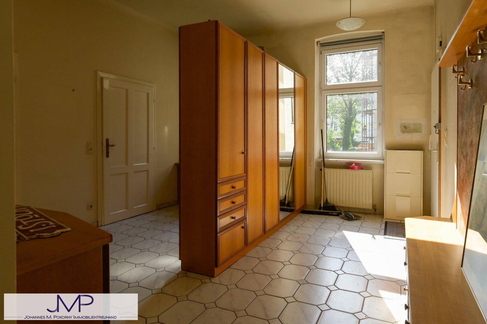 Geräumiger Raum mit Fliesenboden, großem Schrank und Fenster mit Blick ins Grüne.