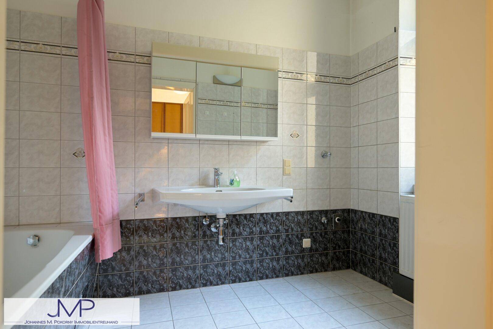 Badezimmer mit Badewanne, Waschbecken und gefliesten Wänden in Schwarz-Weiß, funktional und sauber.