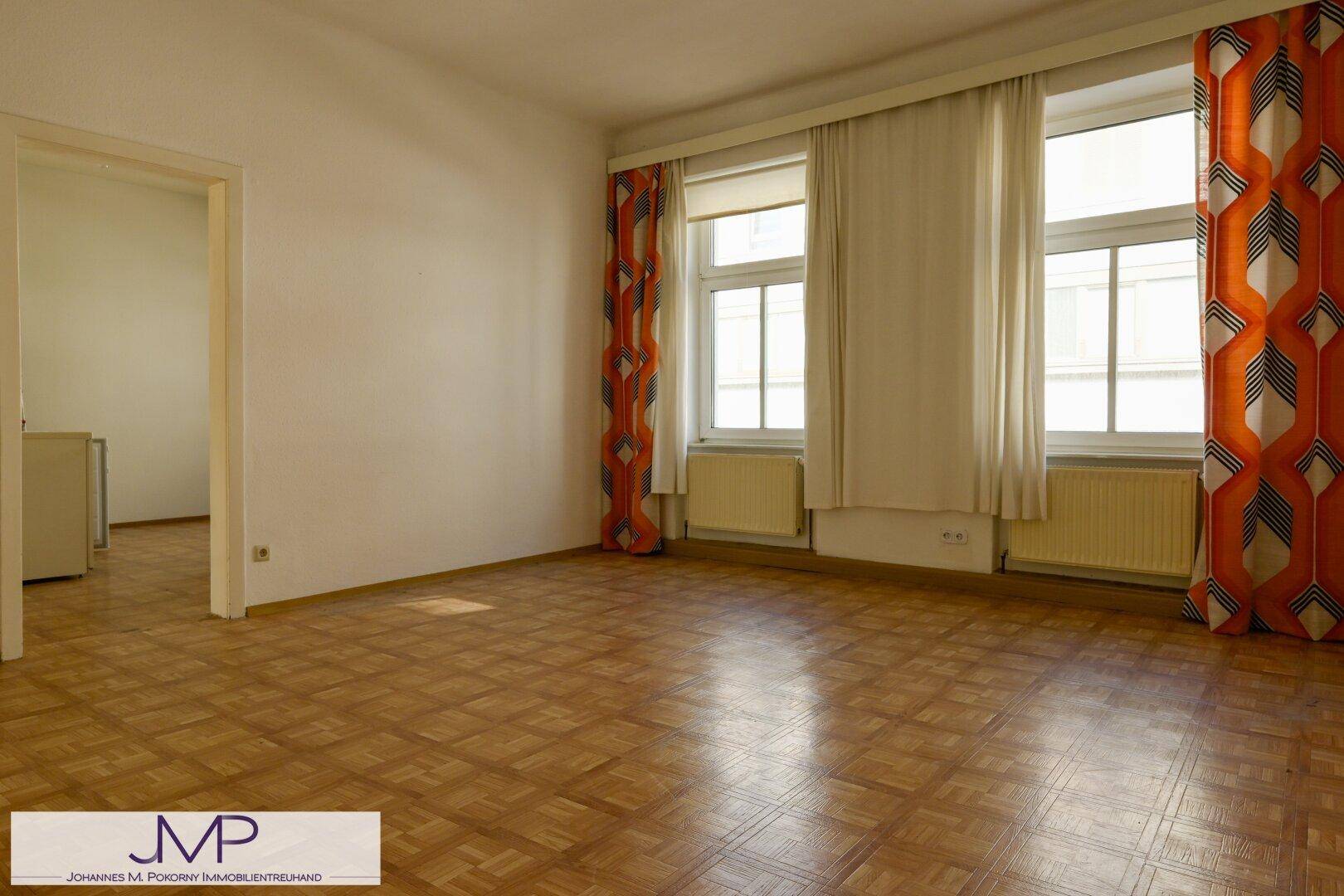 Geräumiges Wohnzimmer mit Parkettboden und zwei großen Fenstern, bietet viel Tageslicht.