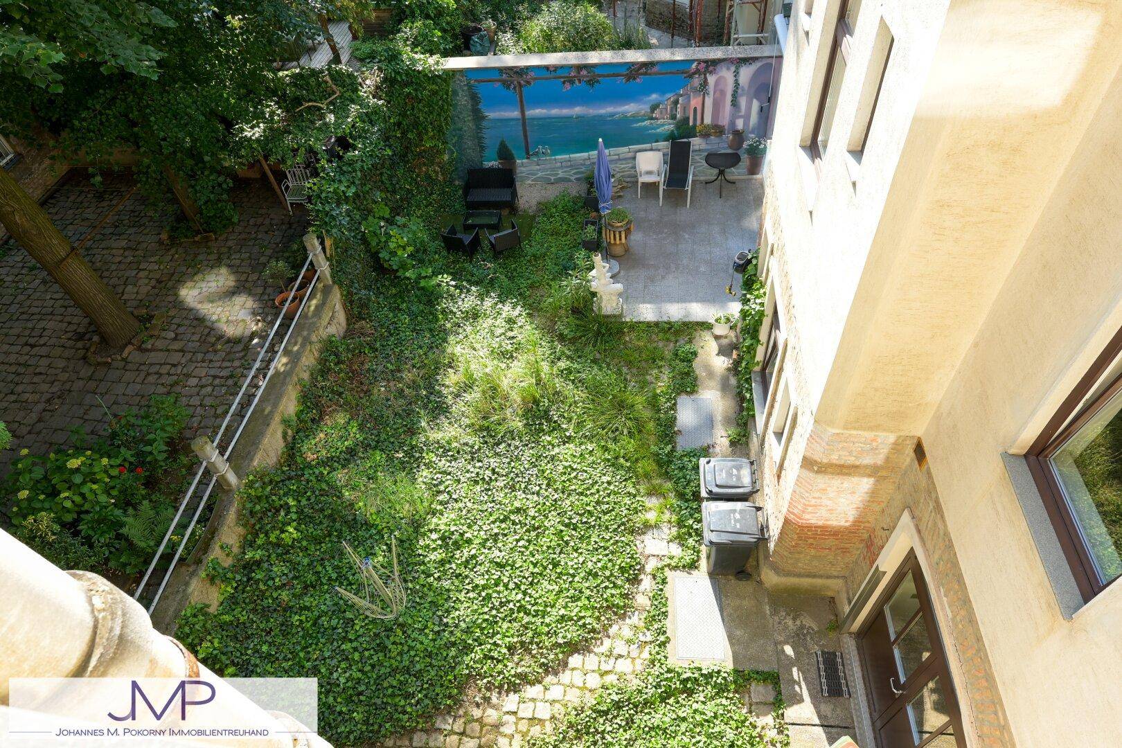 Blick von oben auf den grünen Hinterhofgarten mit Sitzbereich und üppiger Vegetation.