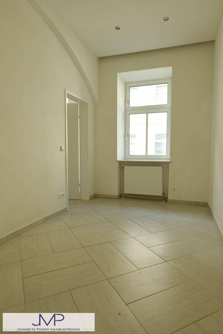 Heller, leerer Raum mit Fliesenboden und einem Fenster, vielseitig nutzbar.