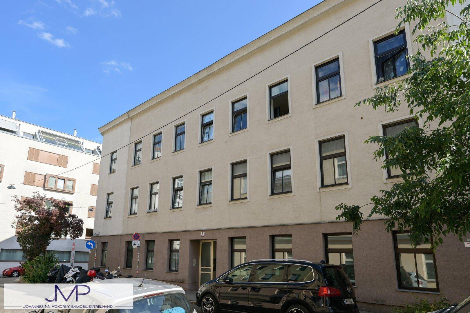 Fassade eines Mehrfamilienhauses mit vielen Fenstern und parkenden Autos auf der Straße.