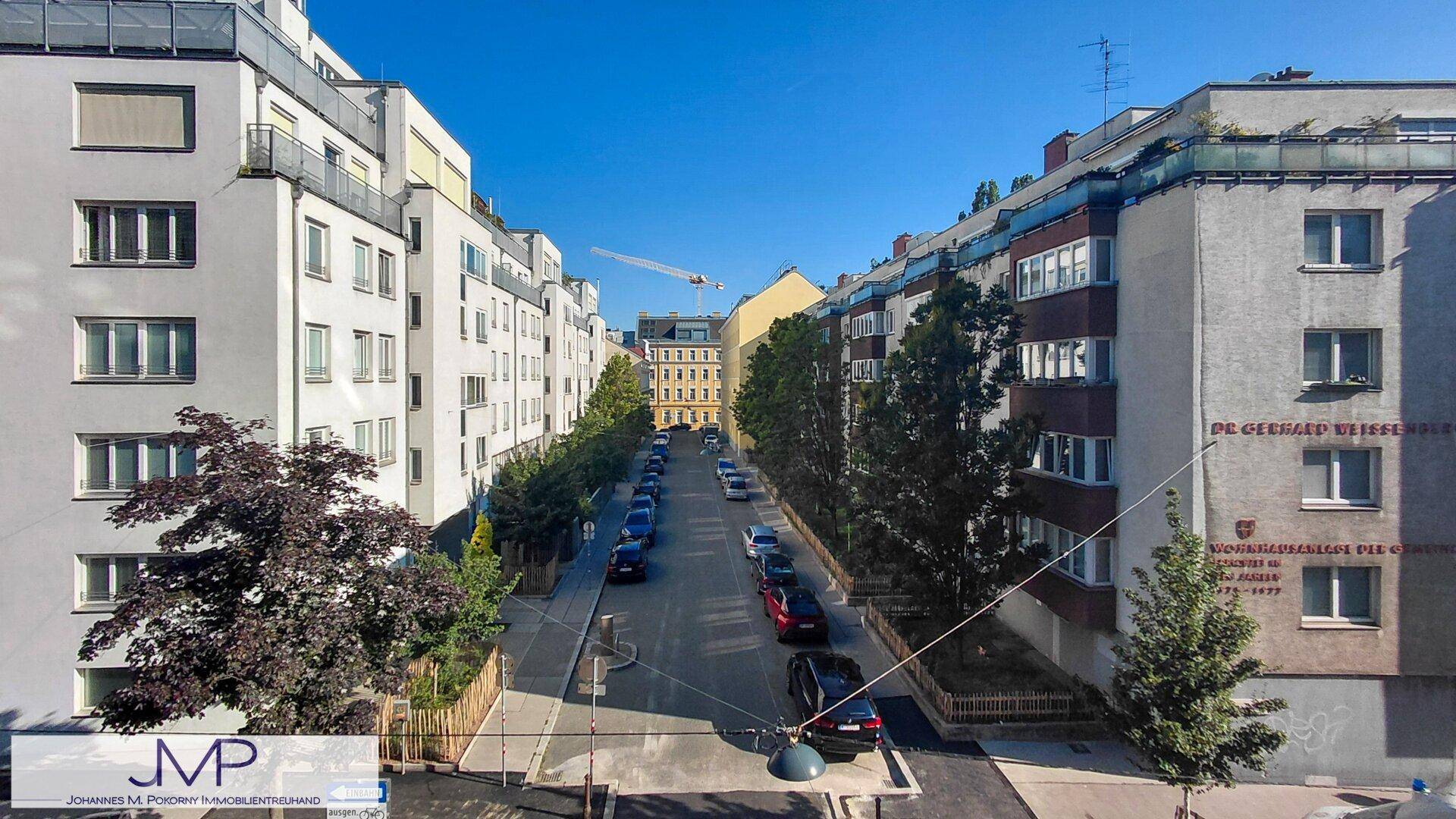 Weitläufiger Blick auf eine ruhige Stadtstraße mit modernen und älteren Gebäuden unter blauem Himmel.