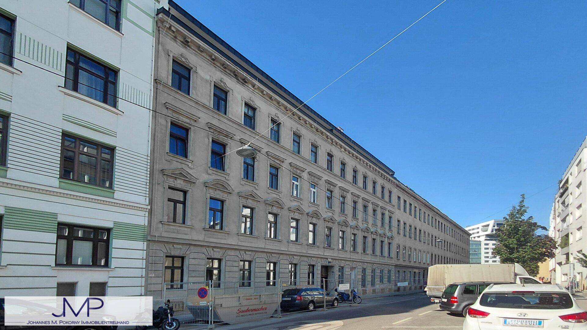 Ansicht einer langen, klassischen Gebäudefassade mit vielen Fenstern und geparkten Autos.