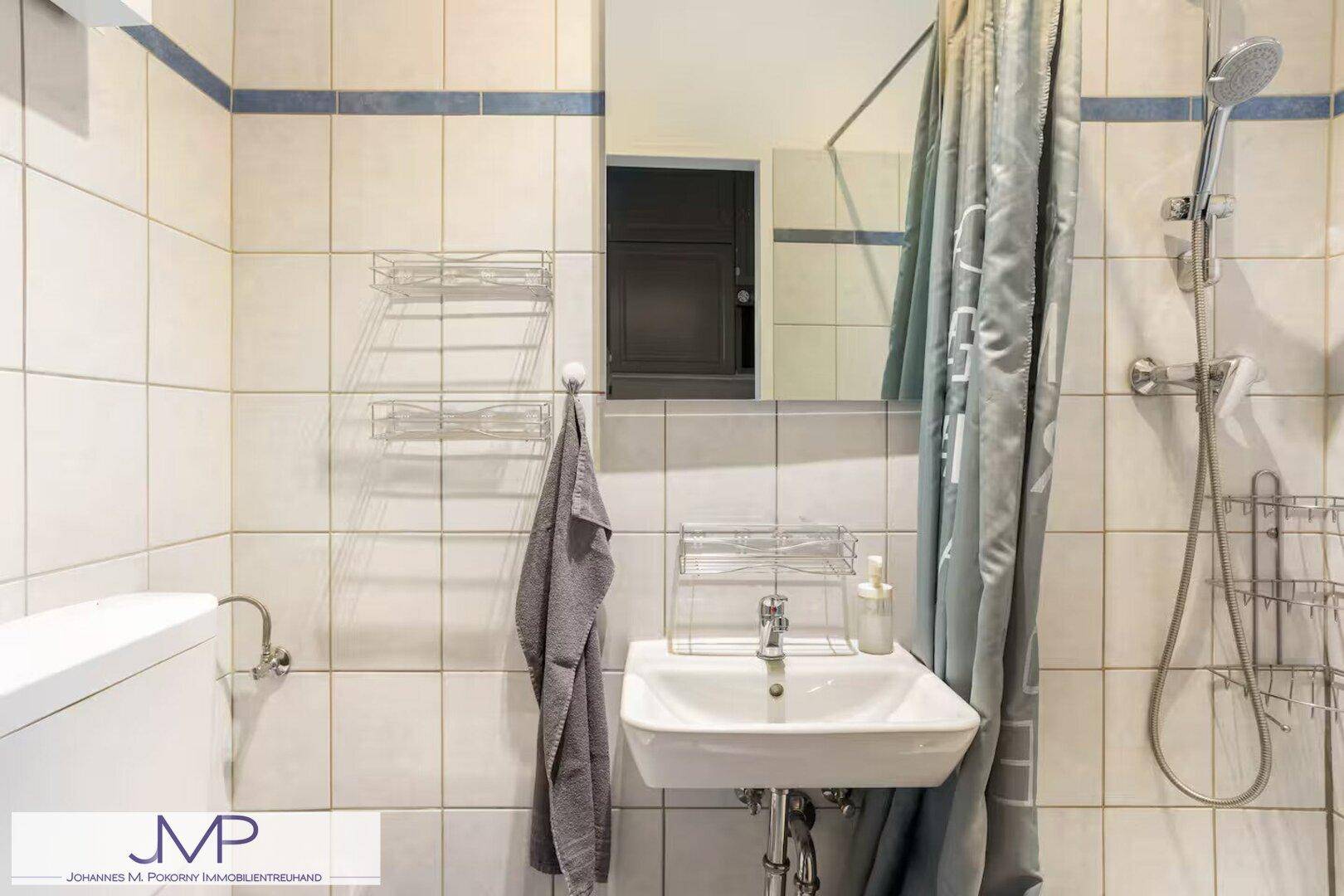 Modernes Badezimmer mit Dusche, Waschbecken und hellen Fliesen.
