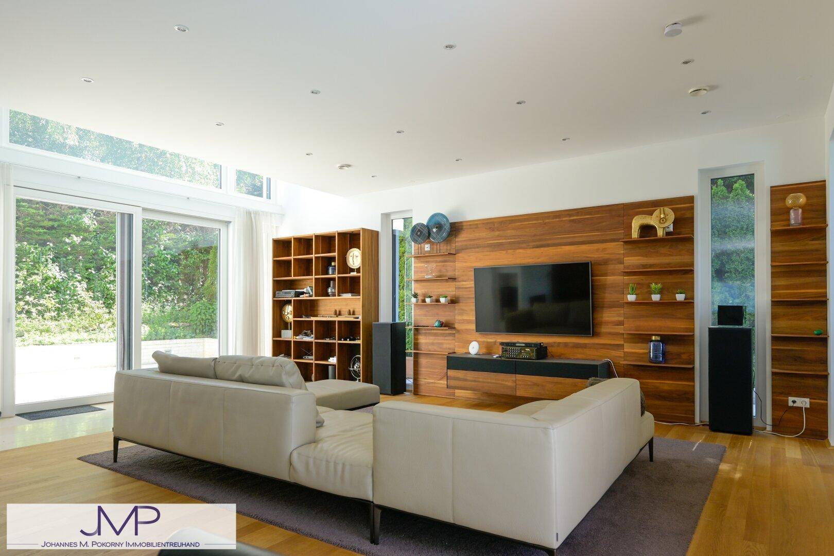 Modernes Wohnzimmer mit Holzwand, großem Fernseher und bequemer Couch, lichtdurchflutet.