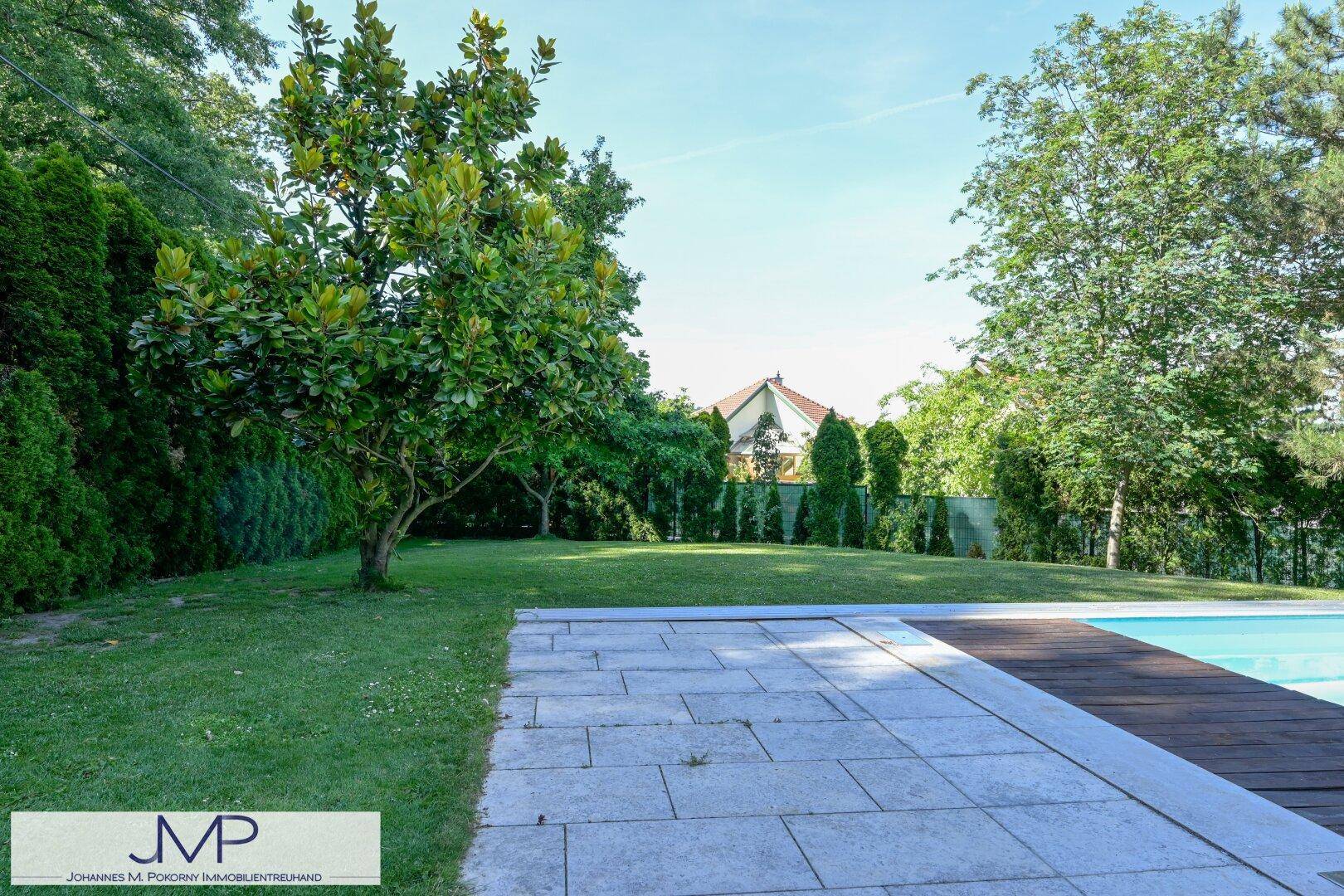 Gepflegter Gartenbereich mit Rasenfläche und angrenzendem Pool, umgeben von Bäumen.
