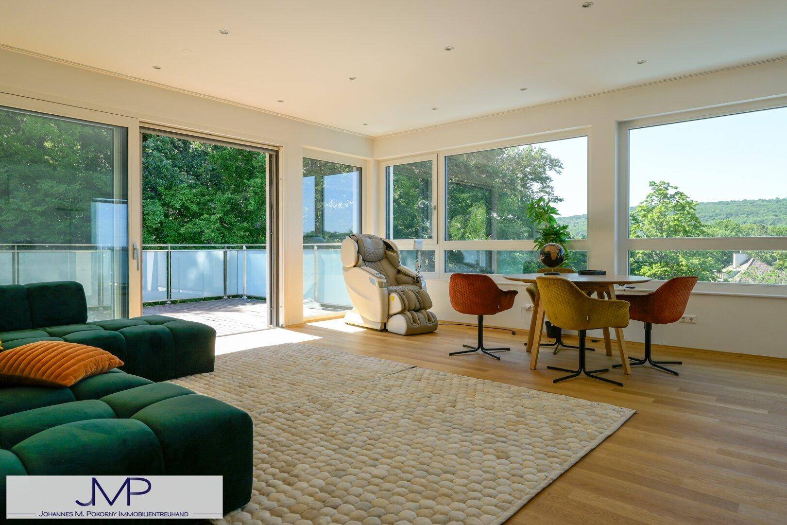 Offener Wohn-Essbereich mit grünem Sofa, Esstisch und großen Fenstern mit Zugang zum Balkon.