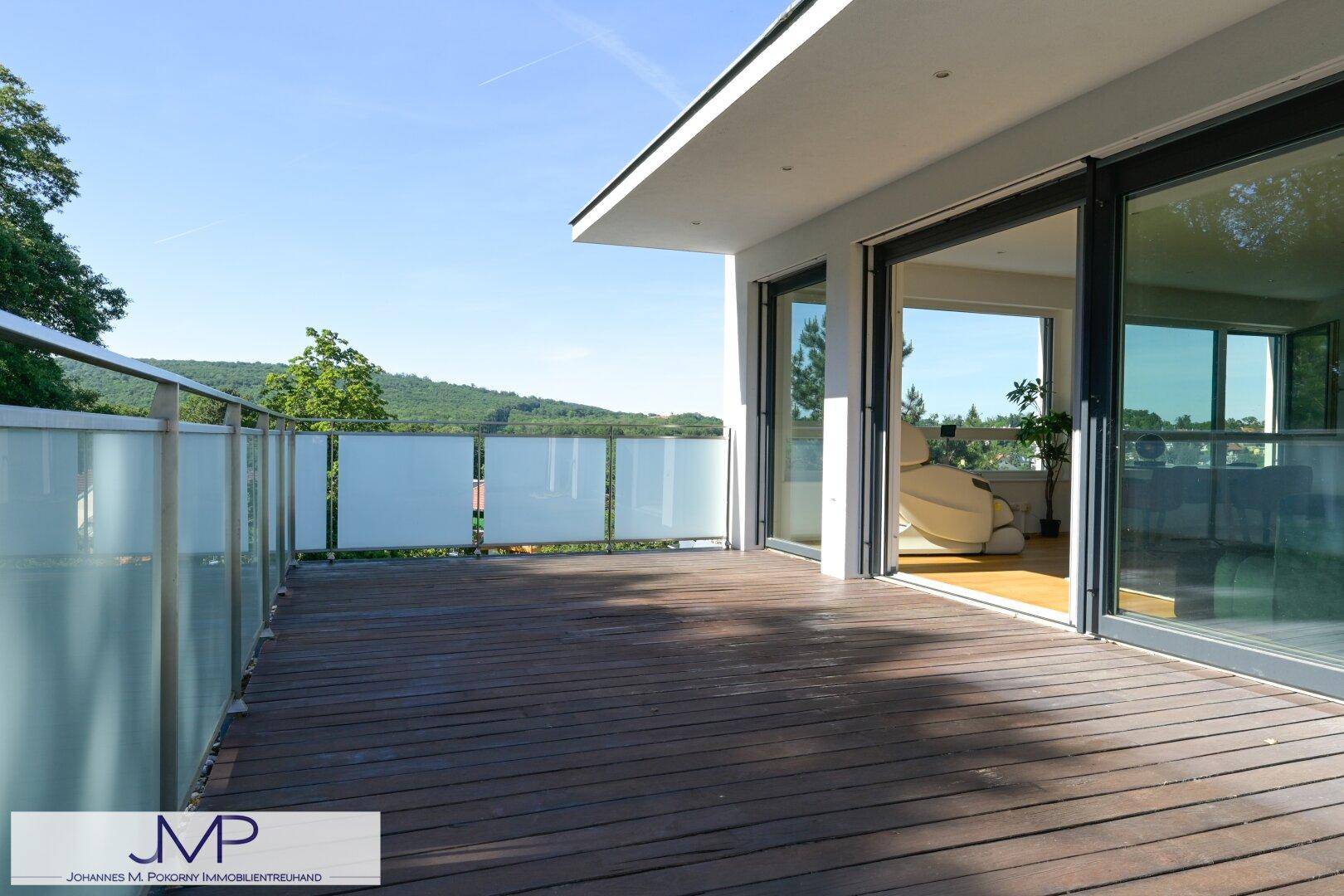 Großer Balkon mit Holzdeck, Glasgeländer und weitem Blick auf die umliegende grüne Landschaft.