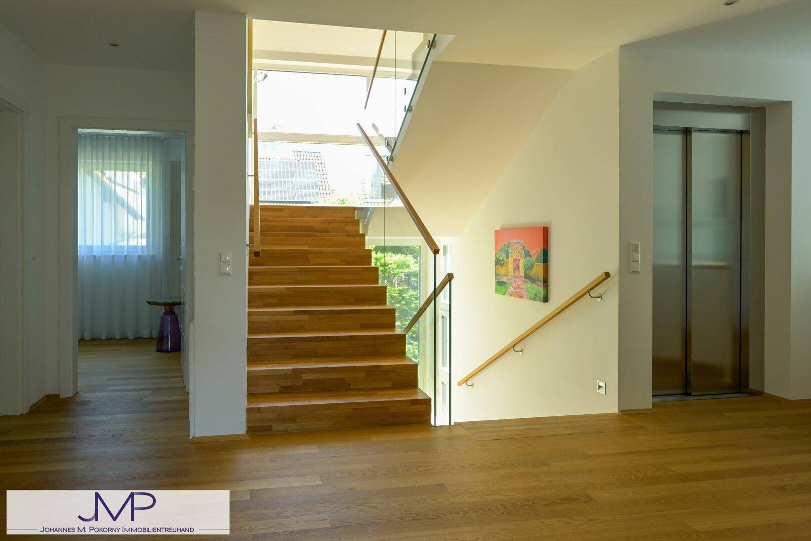Moderner Eingangsbereich mit eleganter Holztreppe, Glasgeländer und integriertem Aufzug für Komfort.
