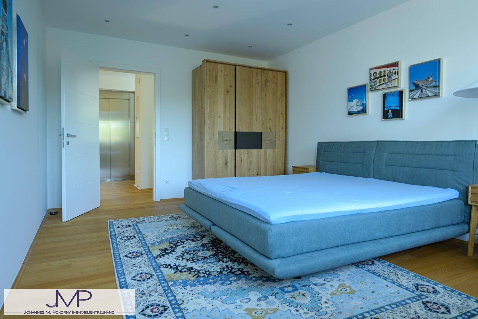 Schlafzimmer mit blauem Bett, Holzschrank und direktem Zugang zum Aufzug im Flur.