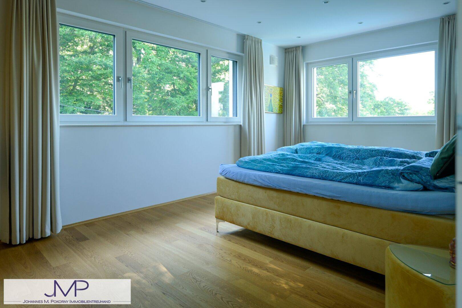 Gemütliches Schlafzimmer mit gelbem Bett und großen Fenstern, die einen schönen Blick ins Grüne bieten.