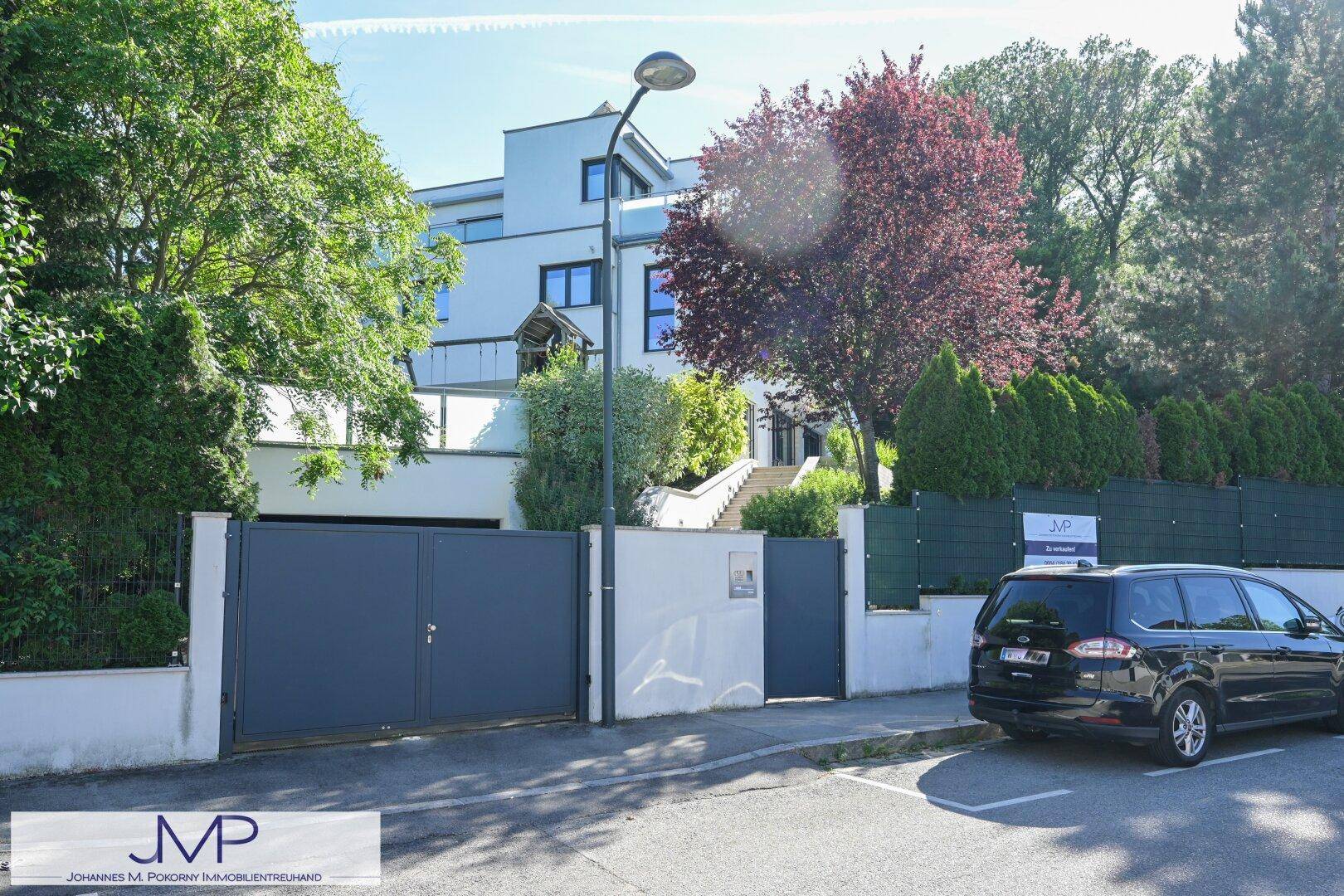 Moderner Hauseingang mit großem Tor, Auffahrt und gepflegter grüner Bepflanzung.