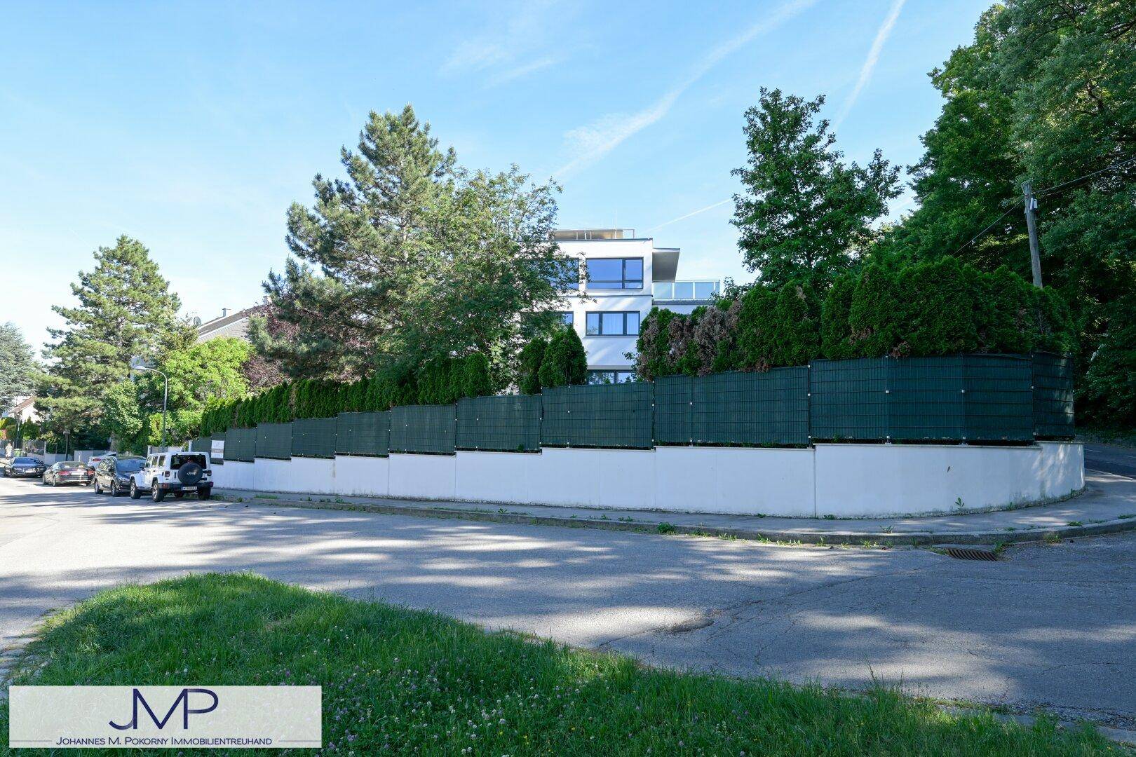 Moderne Wohnanlage mit weißer Fassade, großen Fenstern und grüner Hecke entlang der Straße.
