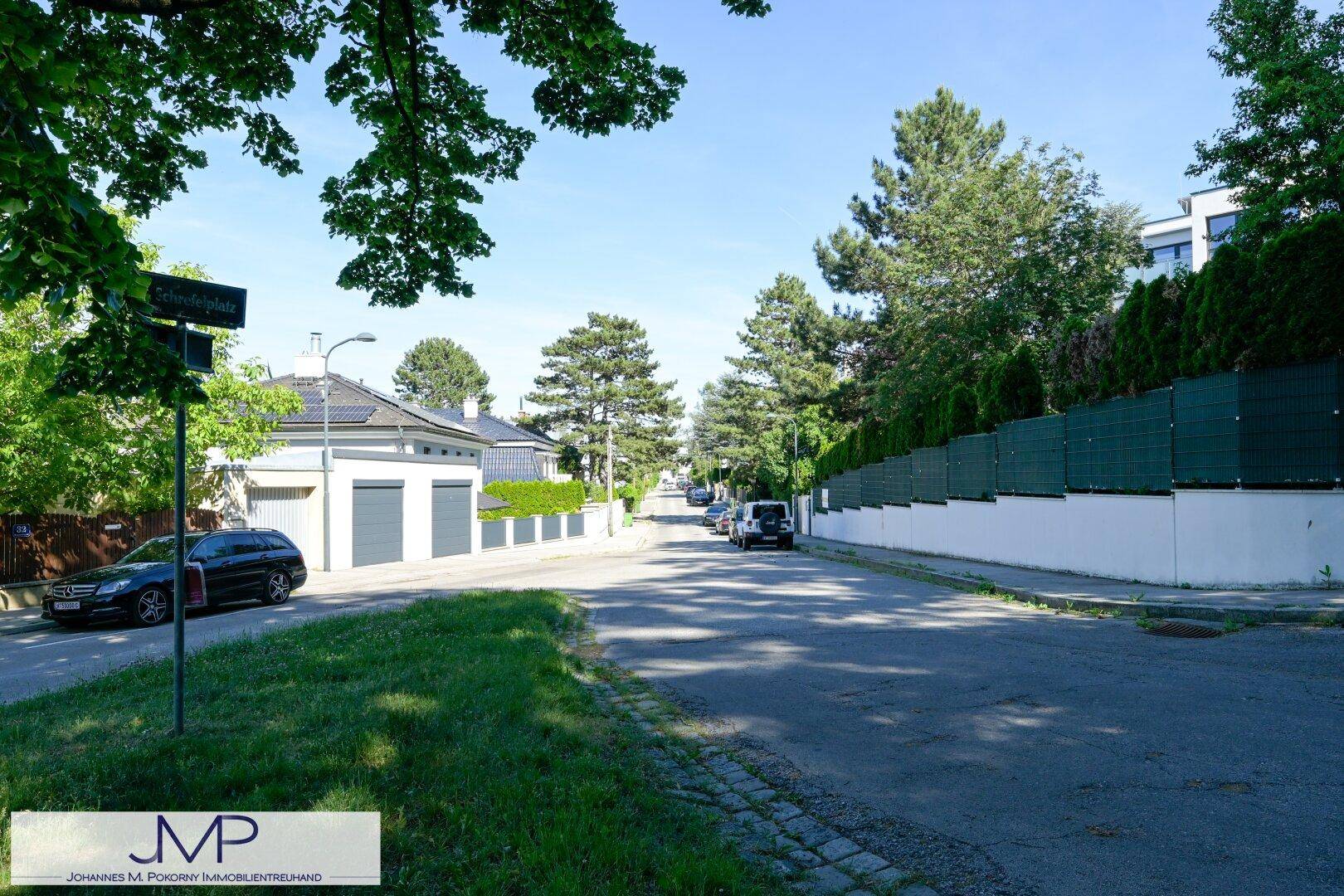 Ruhige Wohnstraße mit gepflegten Häusern, Garagen und viel Grün unter blauem Himmel.