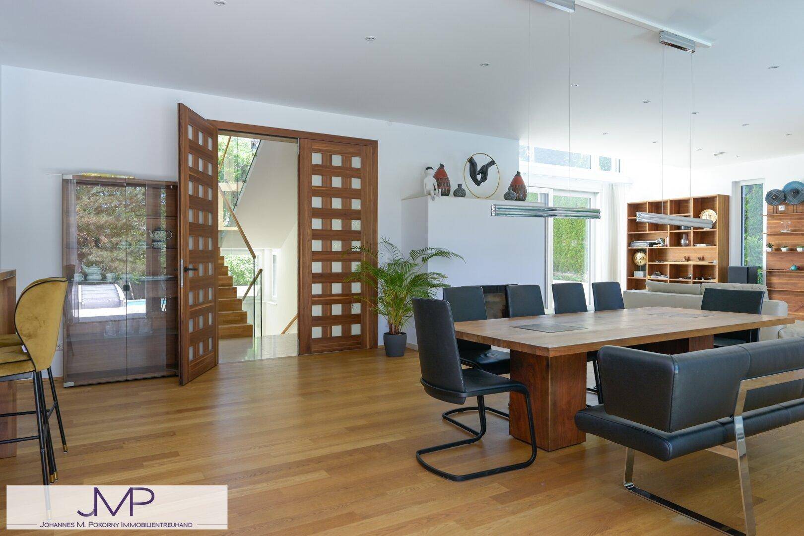 Eleganter Essbereich mit großem Holztisch und Zugang zu einer modernen Treppe.