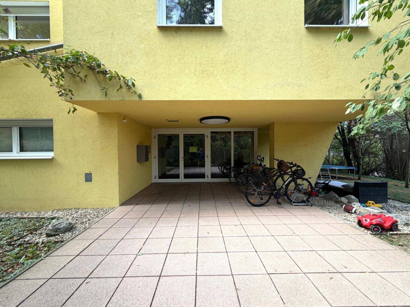 Eingangsbereich des Gebäudes mit gepflastertem Vorplatz und Fahrradabstellmöglichkeiten.