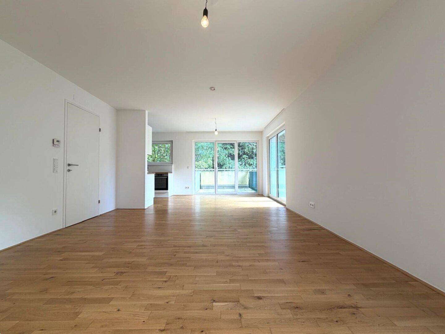 Heller, leerer Wohnbereich mit Holzboden und Zugang zu einem Balkon.