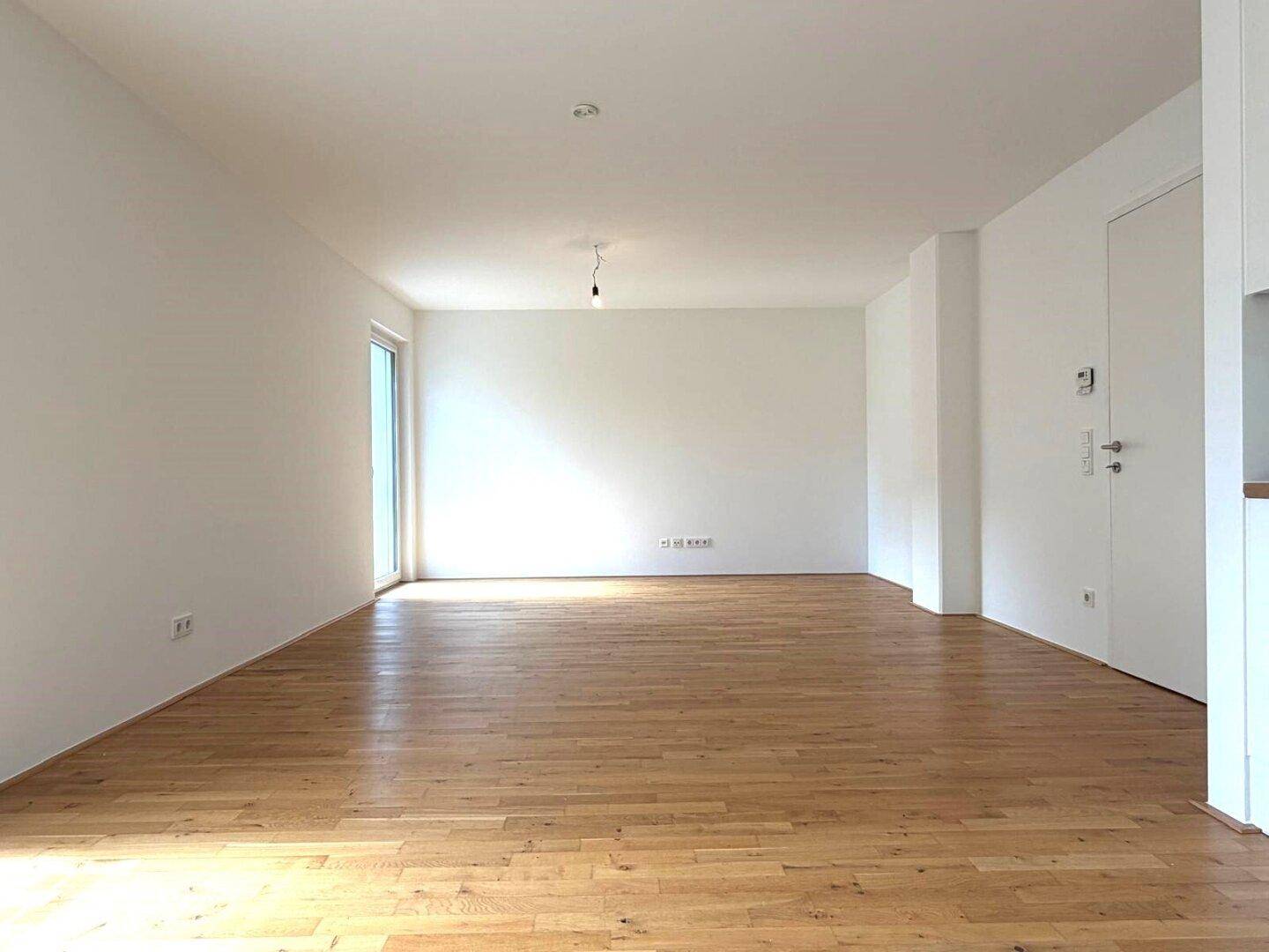 Geräumiger, heller Wohnraum mit Parkettboden und viel Tageslicht durch große Fenster.