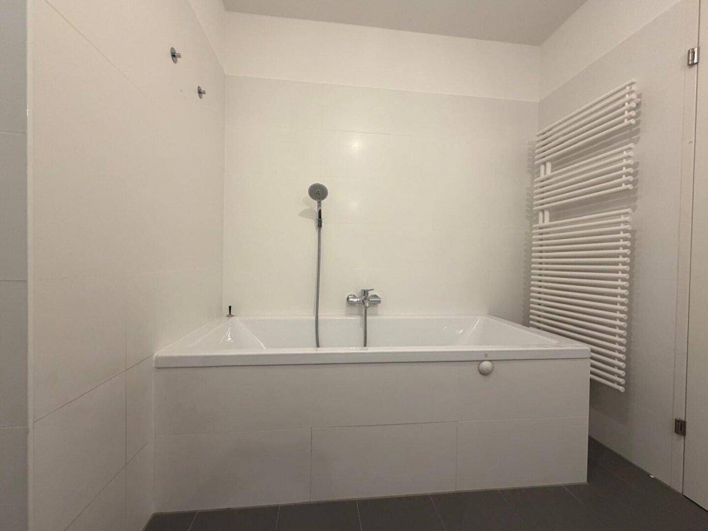 Modernes Badezimmer mit Badewanne, weißen Fliesen und beheiztem Handtuchhalter.