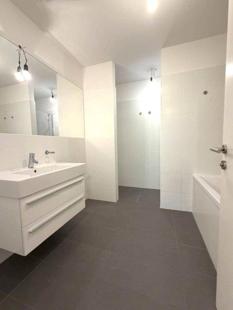 Geräumiges Badezimmer mit modernem Waschtisch, großem Spiegel und dunklen Bodenfliesen.