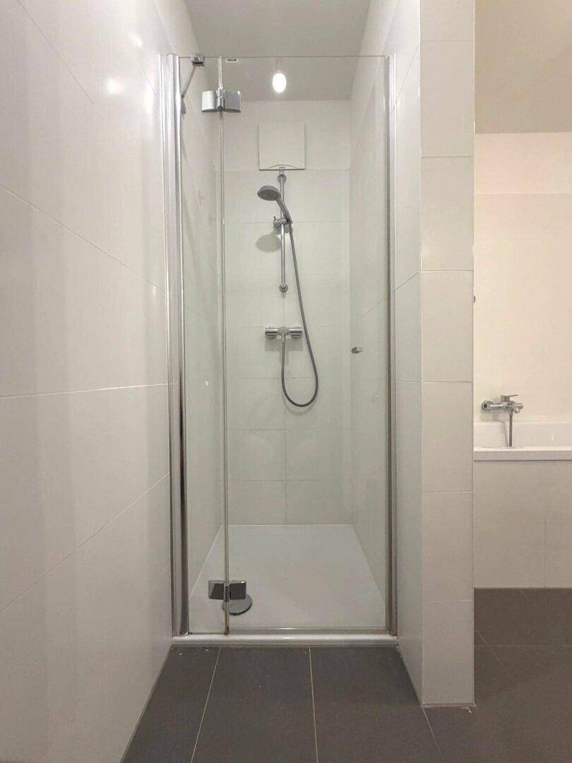 Helles Badezimmer mit moderner Duschkabine und weißen Wandfliesen.