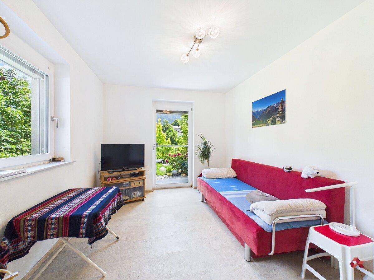 Helles Zimmer mit rotem Schlafsofa und Zugang zum Garten.