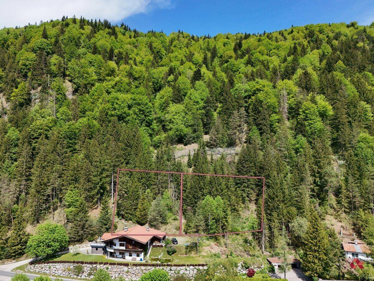 Luftaufnahme eines Hauses am Fuße eines bewaldeten Berges mit markierten Grundstücksgrenzen in der Natur.