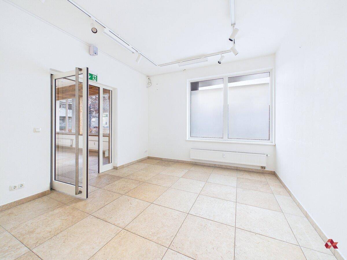 Heller, leerer Raum mit Fliesenboden, großen Fenstern und einer Glastür, ideal für gewerbliche Nutzung.