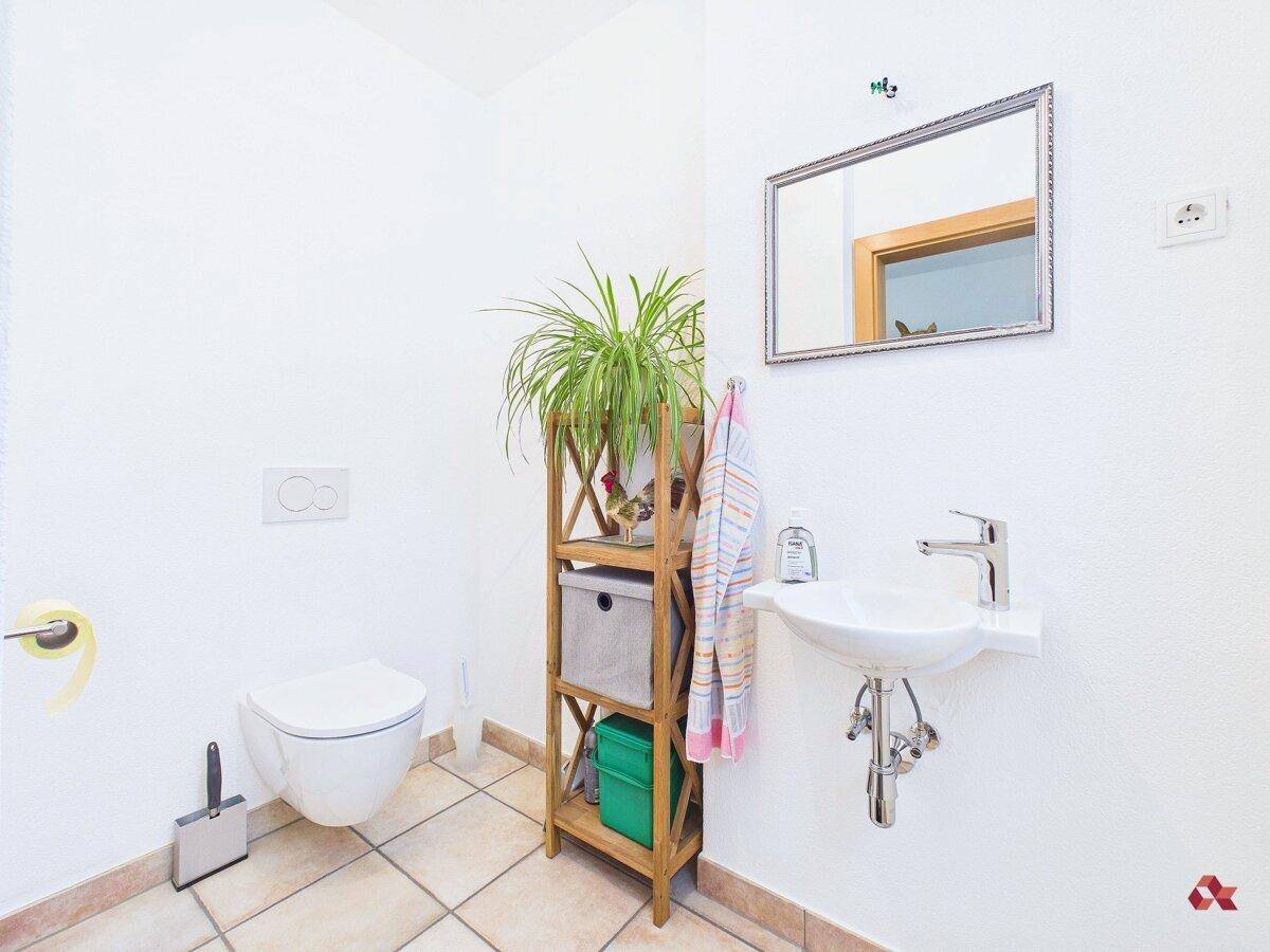 Gäste-WC mit wandhängendem WC, kleinem Waschbecken und Fliesenboden.