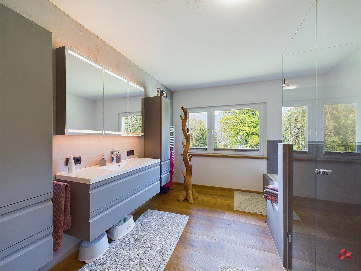Geräumiges Badezimmer mit Doppelwaschbecken, großem Spiegelschrank und Fenster mit Blick ins Grüne.
