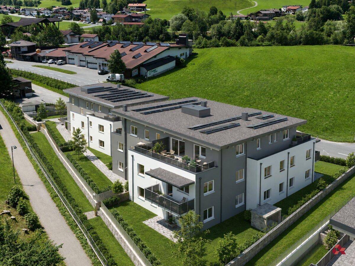 Luftaufnahme einer modernen Wohnanlage mit Flachdach und Photovoltaikanlage in grüner Umgebung.