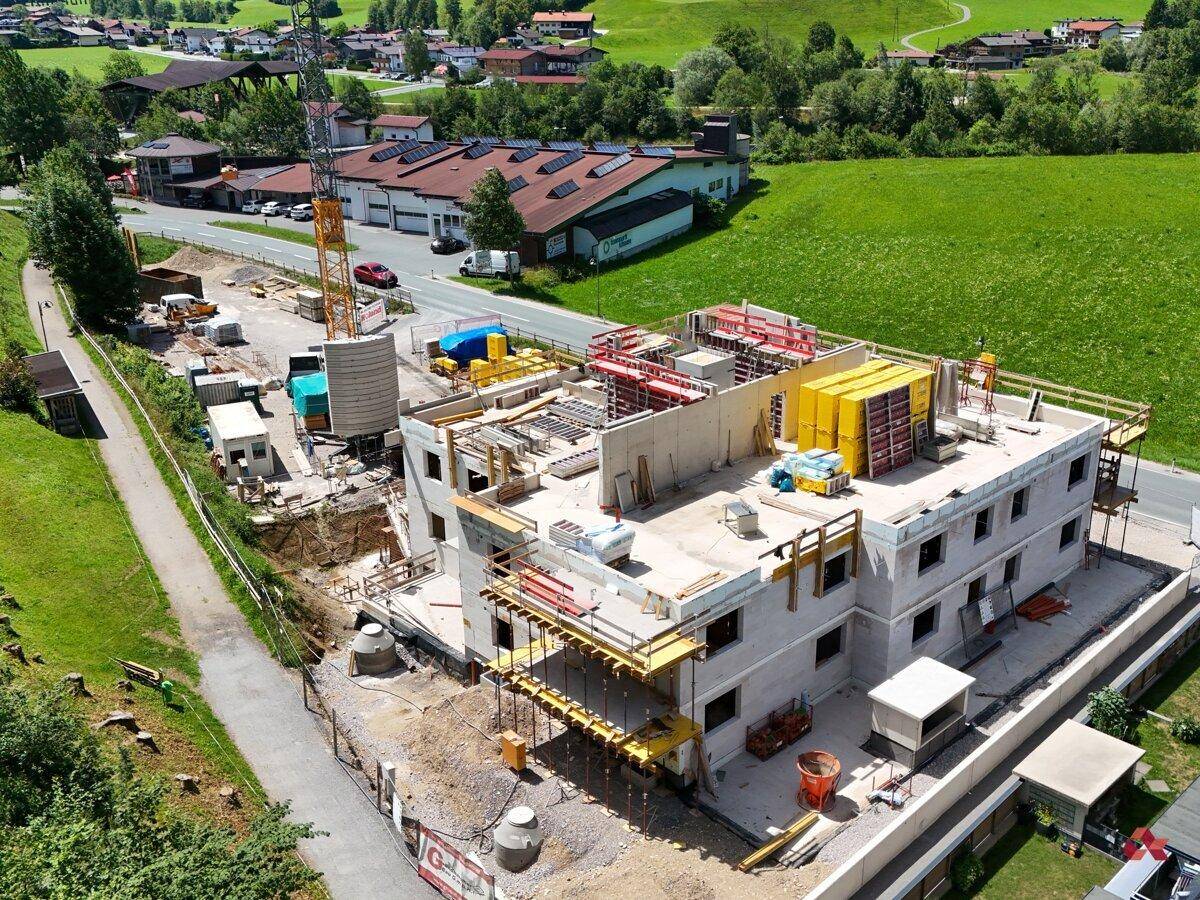 Luftaufnahme einer Baustelle mit Rohbau eines Mehrfamilienhauses und Baukränen in ländlicher Umgebung.