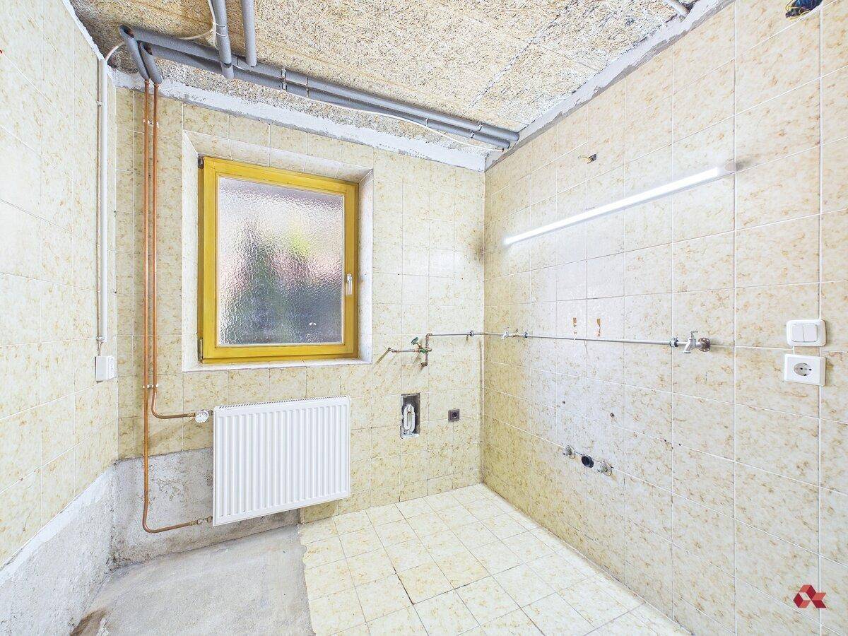 Unfertiger Raum mit Fliesenboden und Heizkörper, ideal als Abstellraum oder Werkstatt.