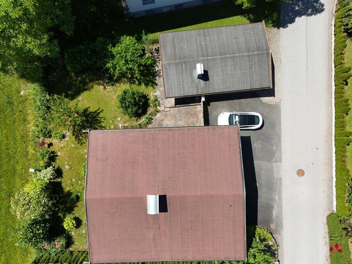 Luftaufnahme von zwei Häusern mit braunen Dächern und einem weißen Auto auf dem Parkplatz daneben.