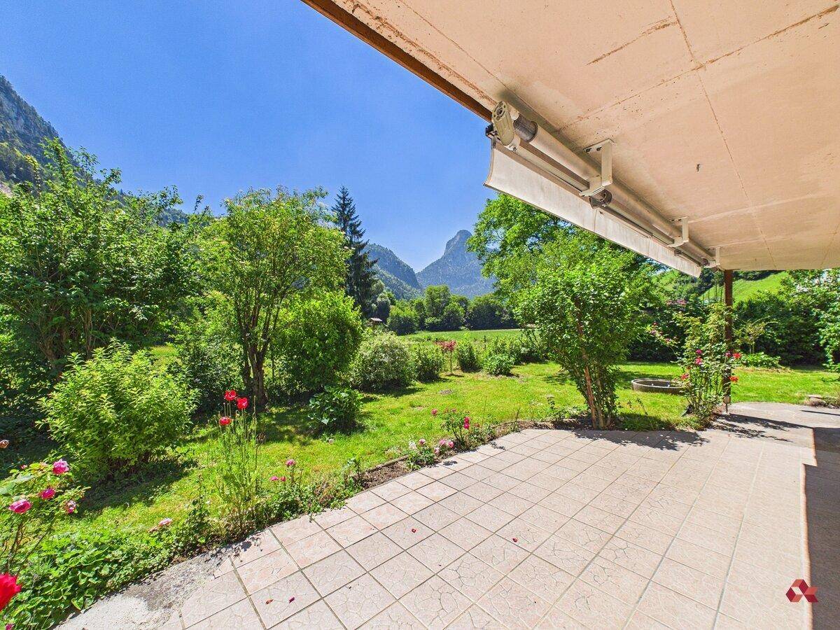 Sonniger Terrassenbereich mit Fliesenboden und weitem Blick über den Garten und die Berge.