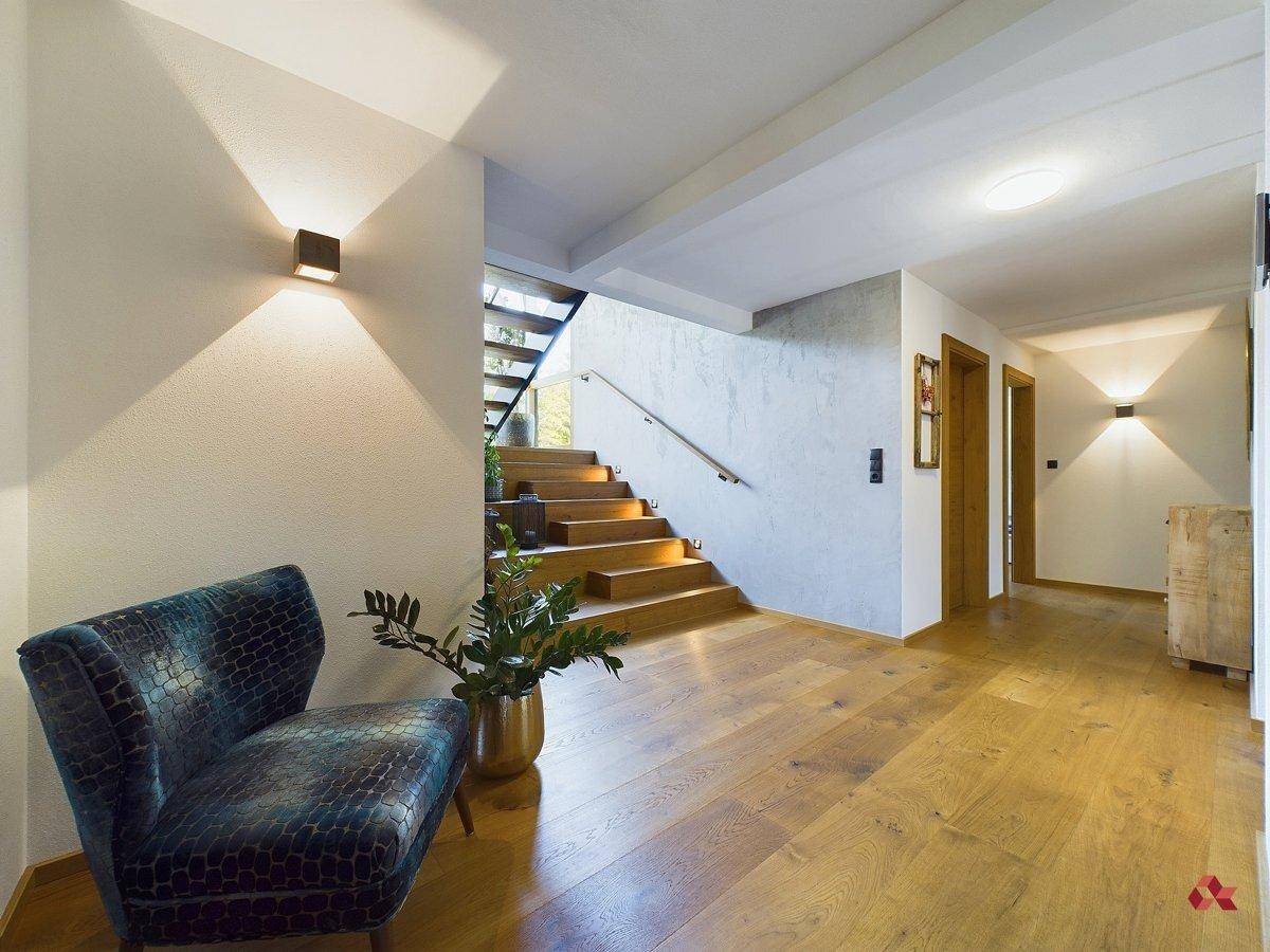 Heller Flur mit elegantem Holzfußboden, offener Holztreppe und gemütlichem Sessel als Blickfang.