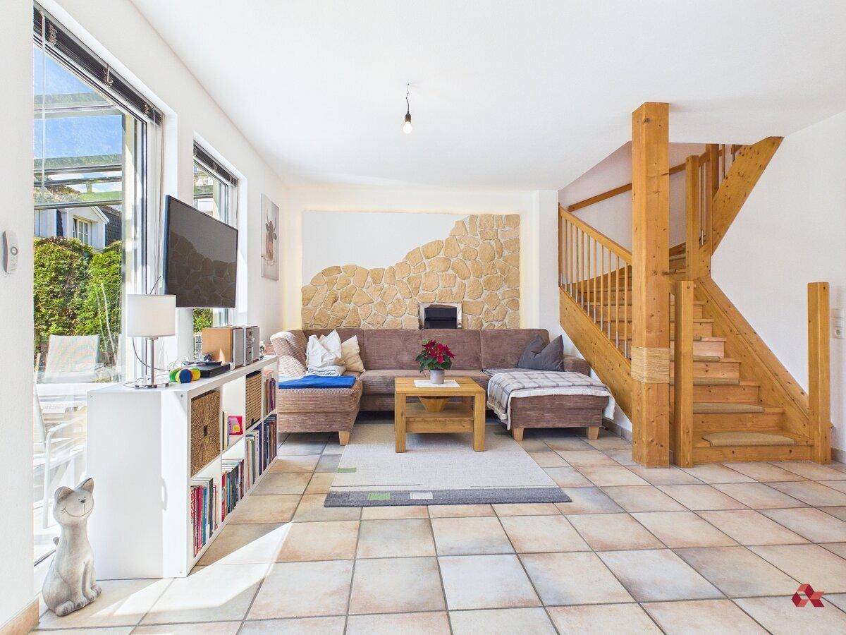Geräumiges Wohnzimmer mit Fliesenboden, Holztreppe und dekorativer Steinwand.