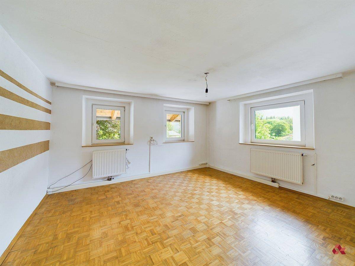 Geräumiges Zimmer mit Parkettboden und drei Fenstern, bietet viel natürliches Licht.