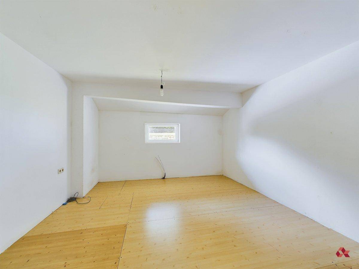 Unfertiger Raum mit Holzboden und kleinem Fenster, ideal für Ausbau oder Lagerung.