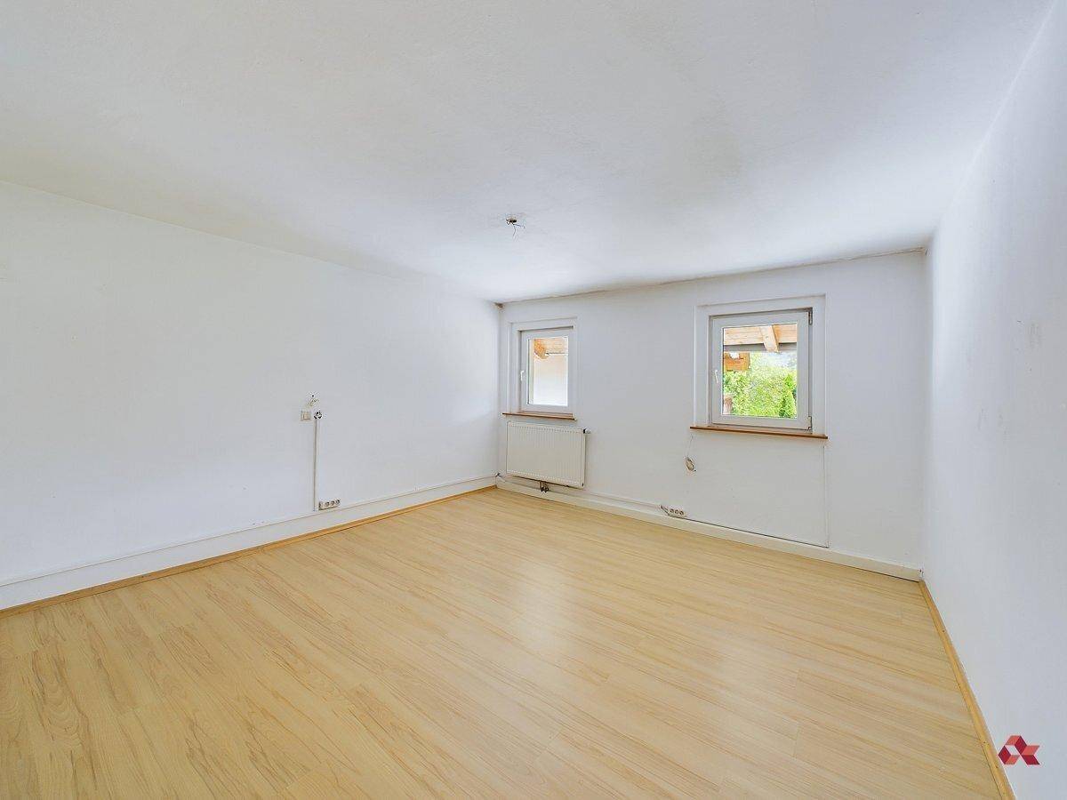 Leeres Zimmer mit hellem Laminatboden und zwei Fenstern, bereit zur individuellen Gestaltung.
